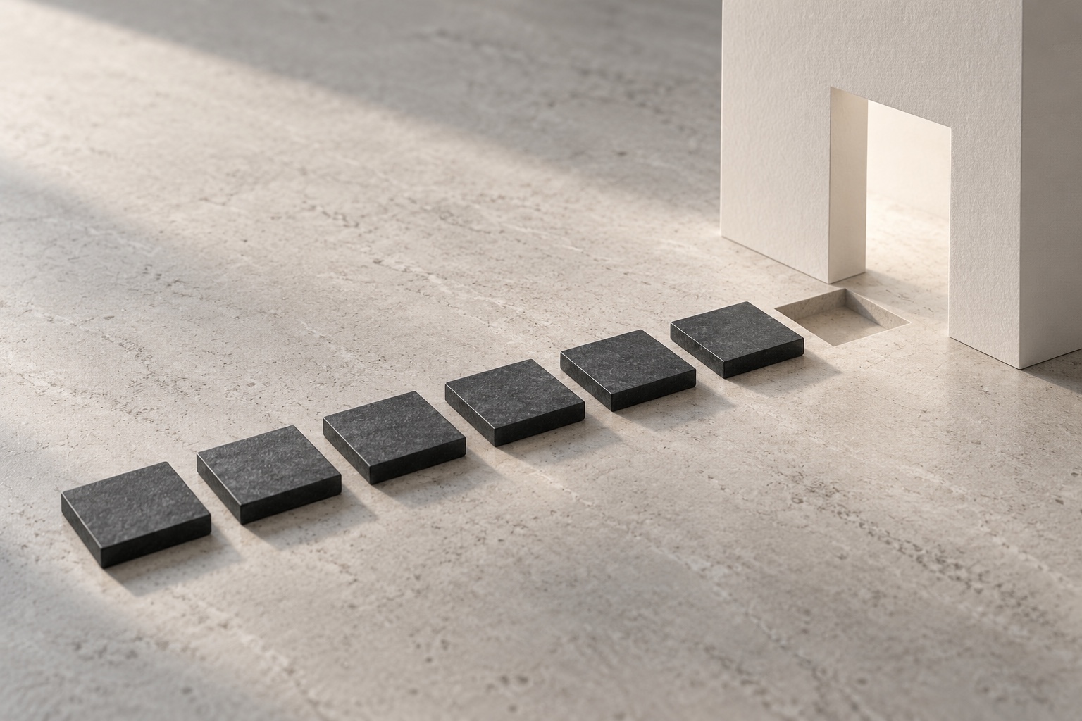 Six matte charcoal stepping tiles on pale stone lead toward a white paper threshold, with one tile resting beside its empty recess.
